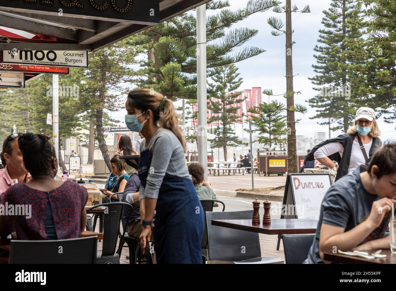 Covid 19, la giovane cameriera indossa un facemark mentre serve i clienti in un ristorante caffetteria a Manly Beach, Sydney, Australia Foto Stock