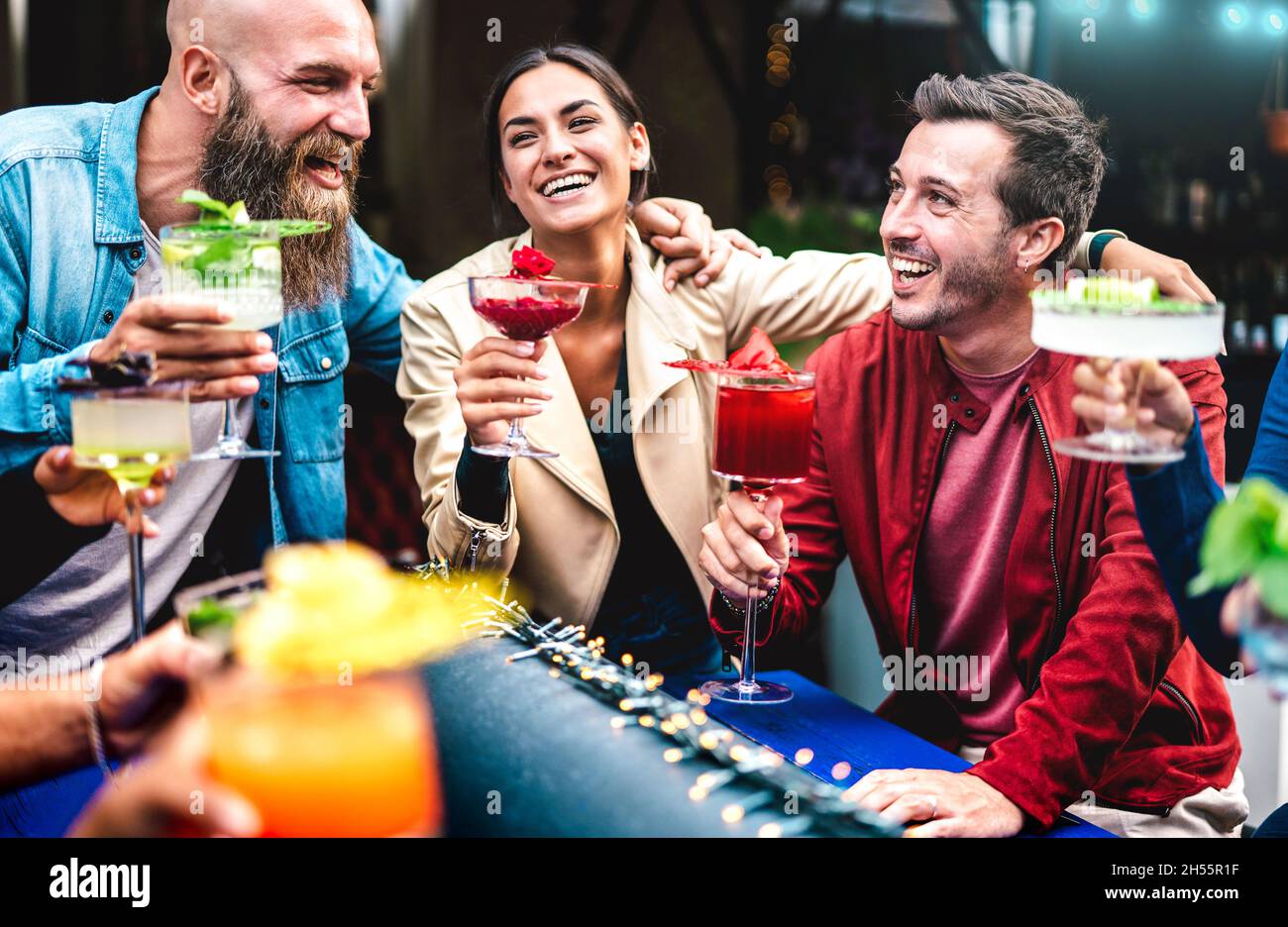 Amici hipster che tostano bevande multicolore al bar alla moda - gente alla moda che si diverte insieme a bere cocktail all'happy hour Foto Stock
