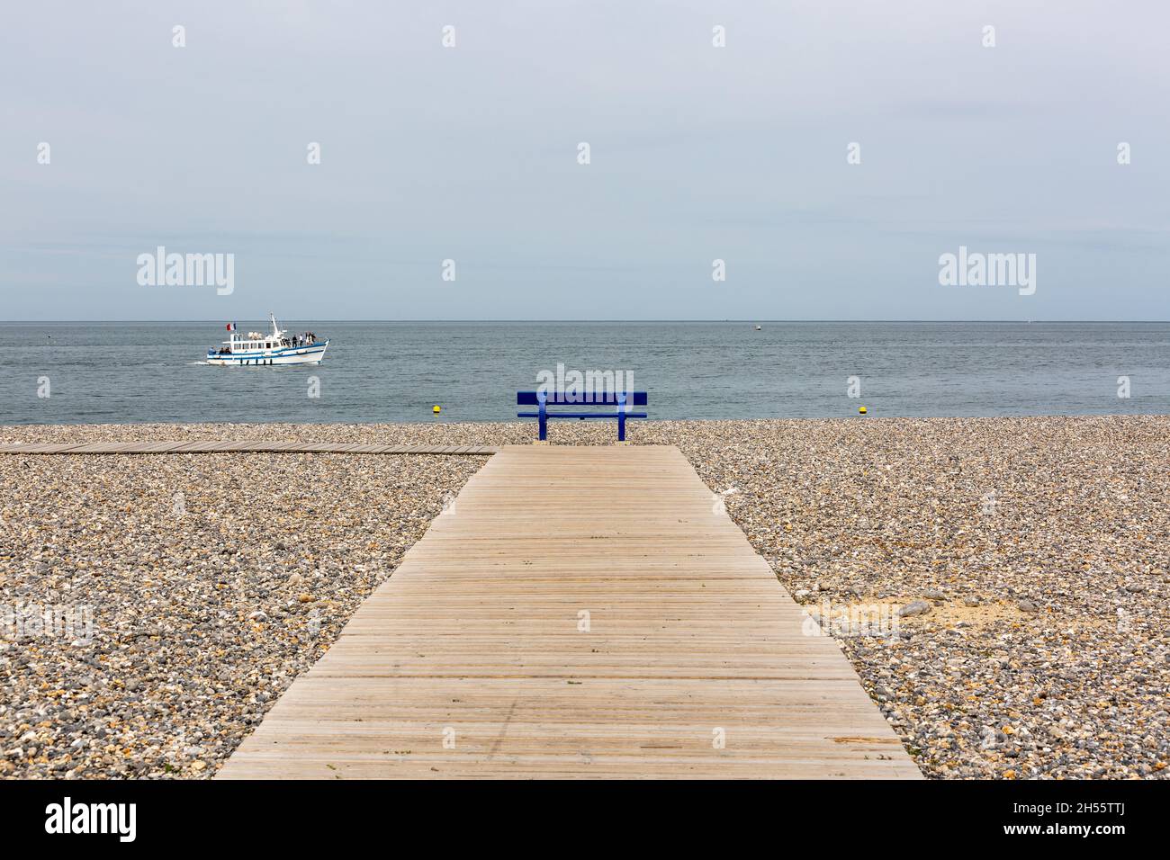 Panca pubblica blu, di fronte al mare, alla fine di un ponte pedonale in legno sulla spiaggia di ciottoli di Tréport, Francia Foto Stock