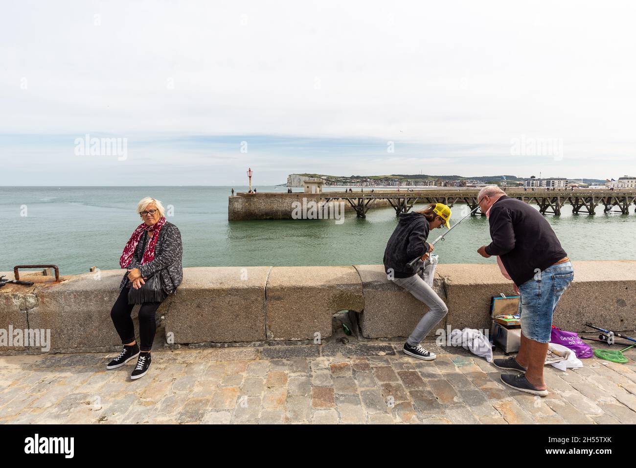 Signora seduto e pescatori su una diga all'ingresso del porto di le Tréport, Francia Foto Stock