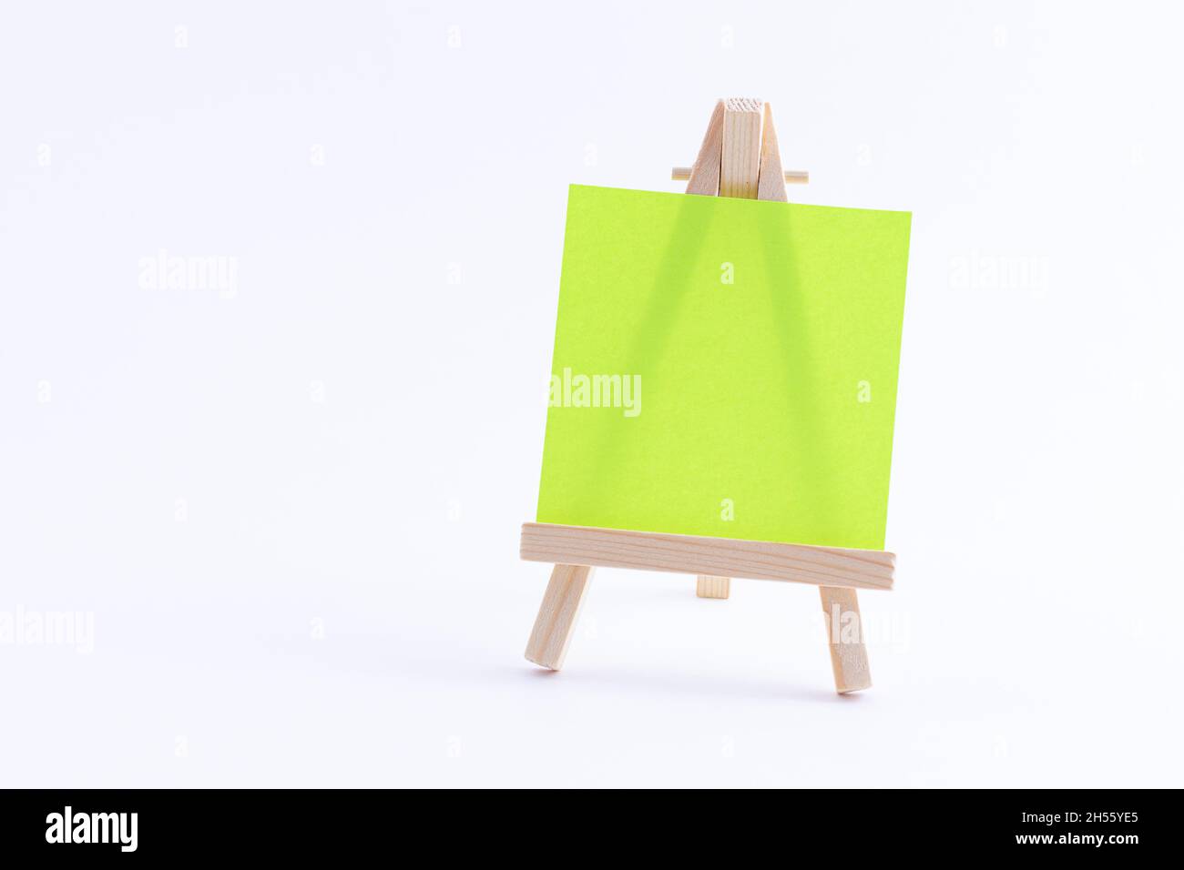 Easel in legno in miniatura con tela quadrata colorata vuota o carta Memo - Mockup. Mini supporto in legno con tavola da disegno pulita su sfondo bianco, spazio per la copia Foto Stock