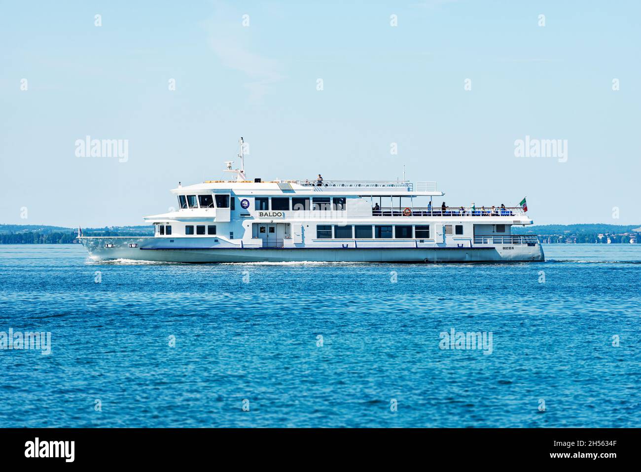 Traghetto bianco chiamato Baldo in navigazione di fronte al piccolo borgo di Bardolino sul Lago di Garda, provincia di Verona, Veneto, Italia. Foto Stock