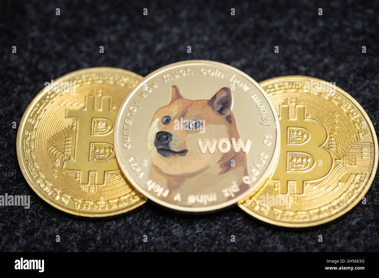 Dogecoin criptovaluta moneta fisica che si stende sopra due monete bitcoin Foto Stock