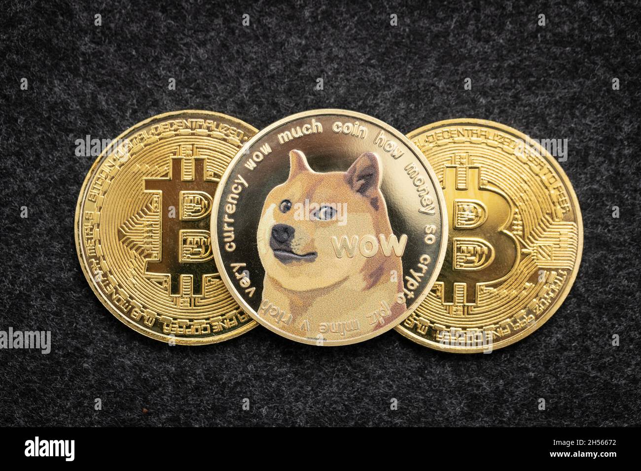Dogecoin criptovaluta moneta fisica che si stende sopra due monete bitcoin Foto Stock