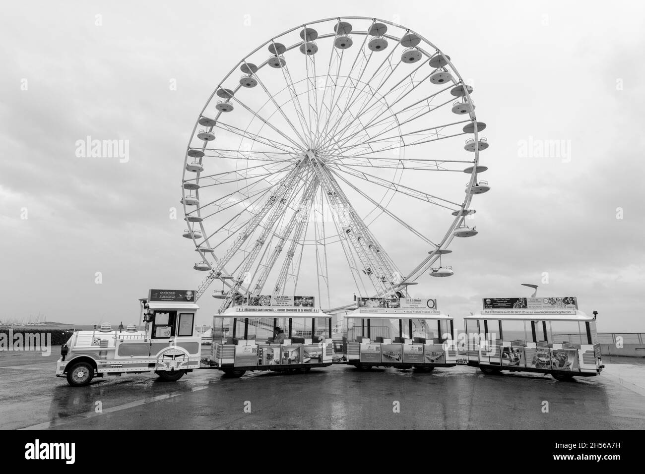 Immagine in bianco e nero della ruota panoramica e del mini treno sotto la pioggia a Saint-Raphael, Var, Costa Azzurra, Francia. Foto Stock