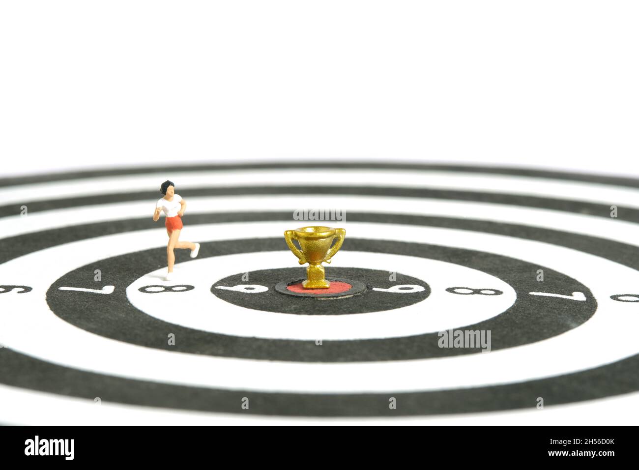 Fotografia di personaggi giocattolo in miniatura. Vincere un concetto di gara di corsa. Un runner che corre sopra la tavola da disegno con trofeo d'oro al centro, isolare Foto Stock