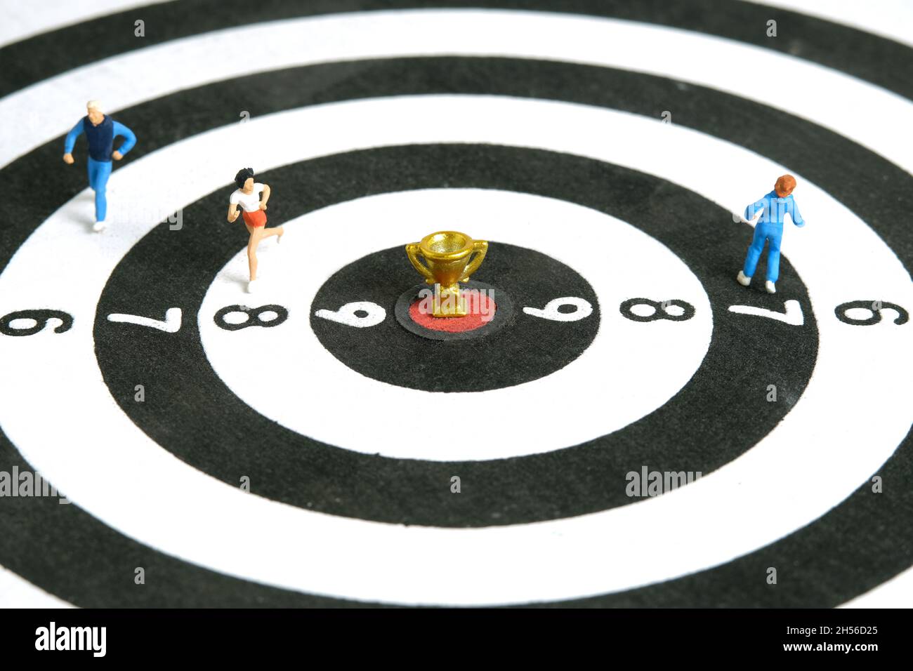 Fotografia di personaggi giocattolo in miniatura. Vincere un concetto di gara di corsa. Un runner che corre sopra la tavola da disegno con trofeo d'oro al centro, isolare Foto Stock