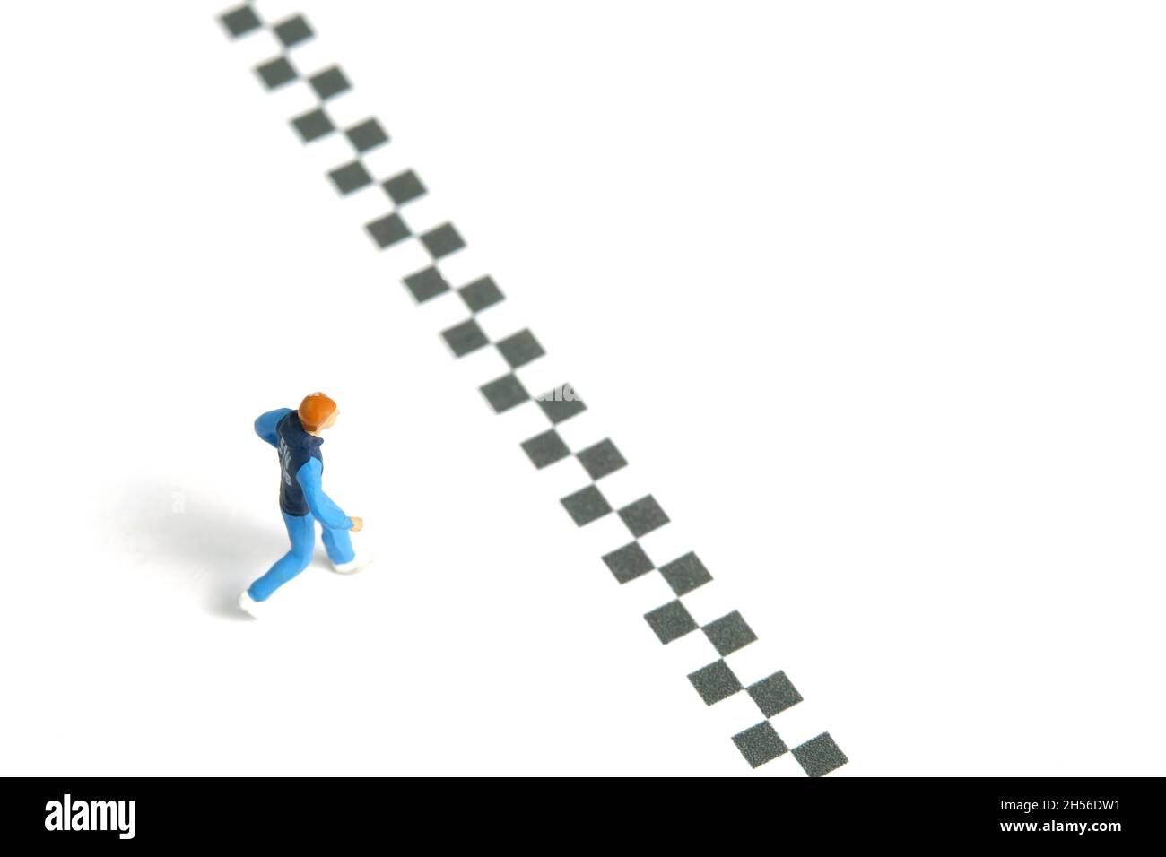 Fotografia di personaggi giocattolo in miniatura. Un giovane che corre verso il traguardo, isolato su sfondo bianco. Foto immagine Foto Stock