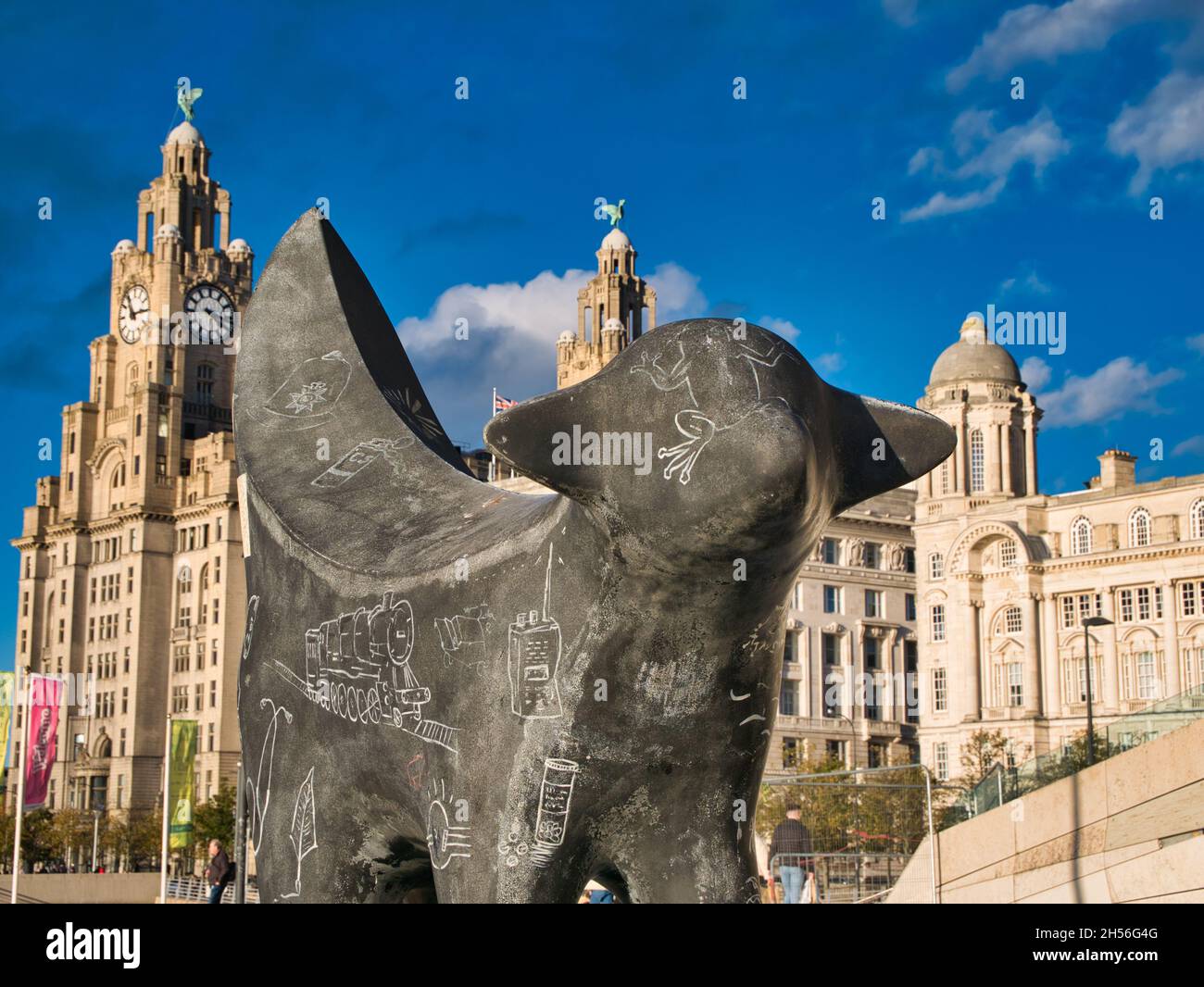 Una statua di SuperLambBanana al Pier Head sul fiume Mersey a Liverpool. Il Liver Building appare sullo sfondo in una giornata di sole con cielo blu. Foto Stock