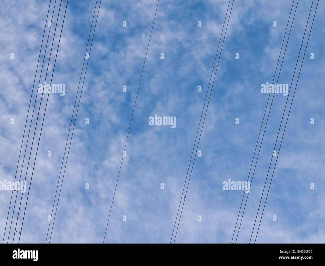 Cavi di trasmissione dell'elettricità ad alta tensione sospesi - parte della rete nazionale del Regno Unito - contro un cielo blu con nuvole bianche. Foto Stock