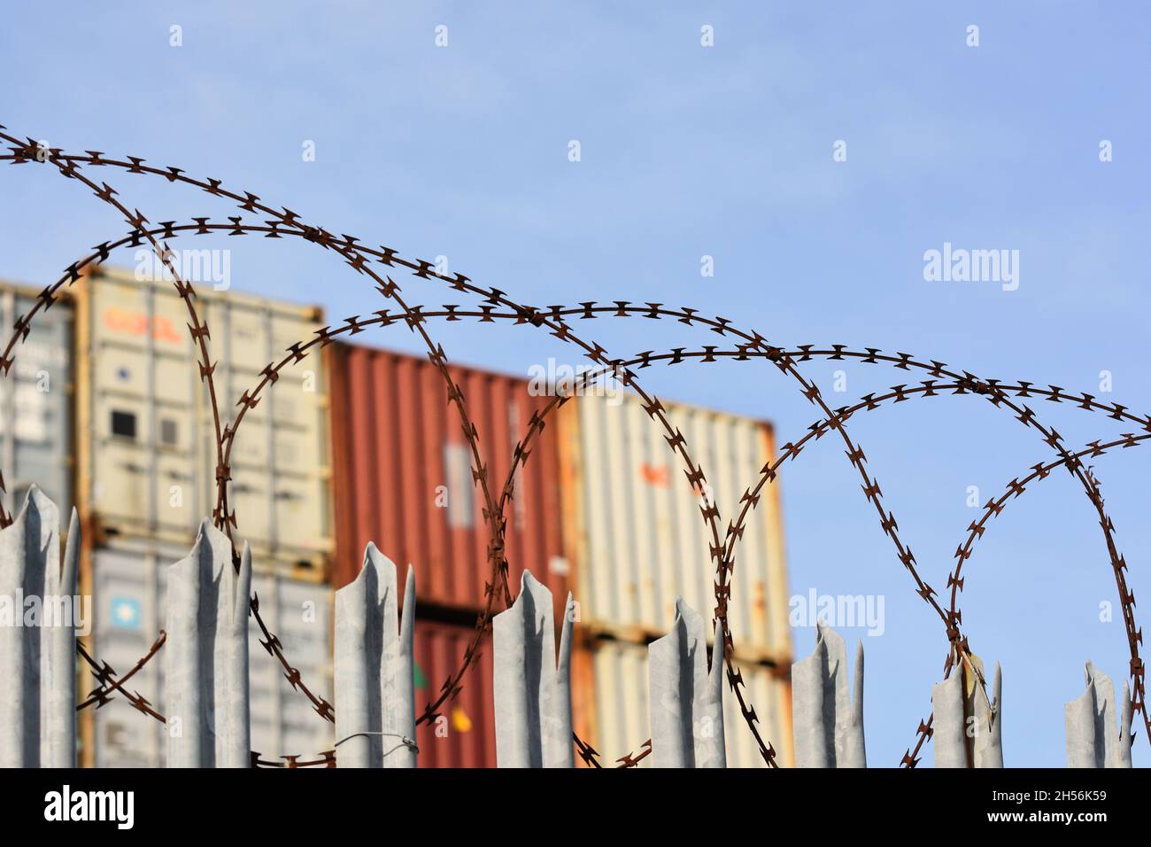 I contenitori per la spedizione di merci si sono accatastati dietro una recinzione con un filo spinato in cima a uno dei porti più trafficati del Regno Unito a Southampton. Foto Stock