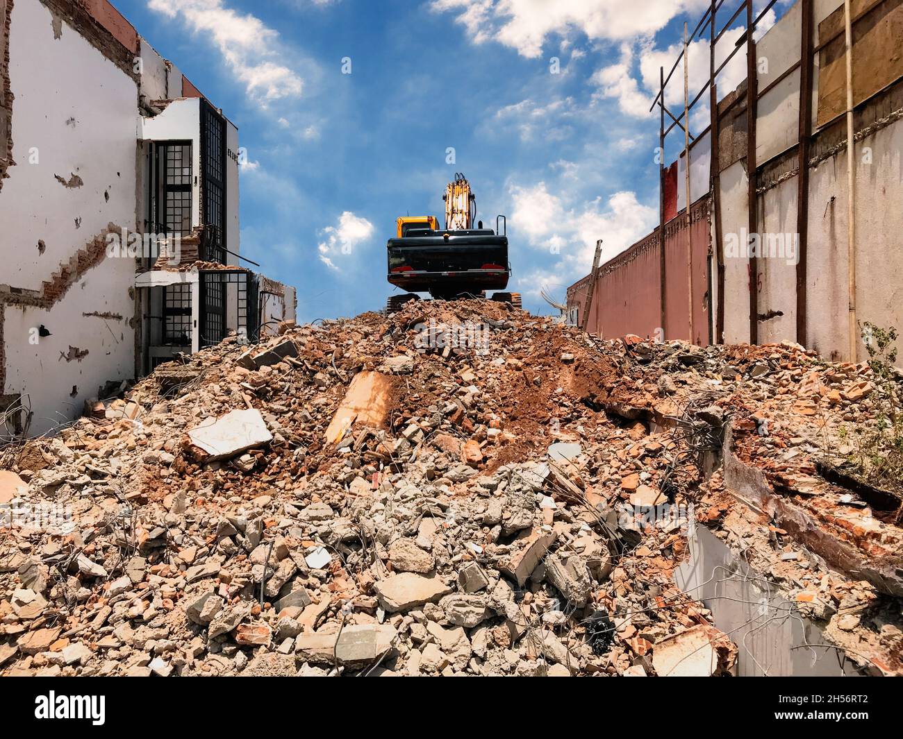 Demolizione di edifici. L'escavatore rompe la vecchia casa in un giorno di tramonto nuvoloso. Liberare spazio per la costruzione di un nuovo edificio Foto Stock