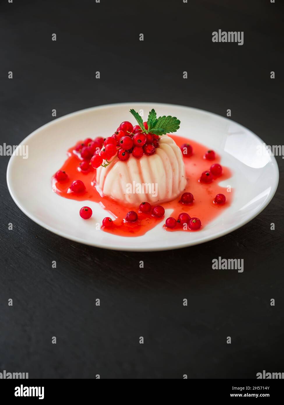 Gelatina di cocco con bacche estive. Panna cotta con bacche di ribes in piatto bianco. Foto Stock