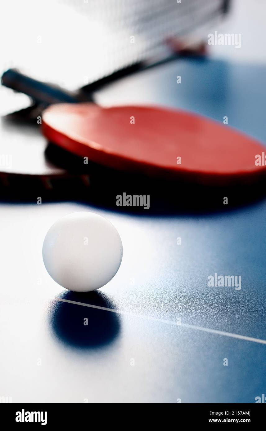 Due racchette da tennis e una palla bianca si trovano su un tavolo da tennis vicino alla rete. Attività ricreative attive e giocare a ping pong. Background sportivo. Foto Stock