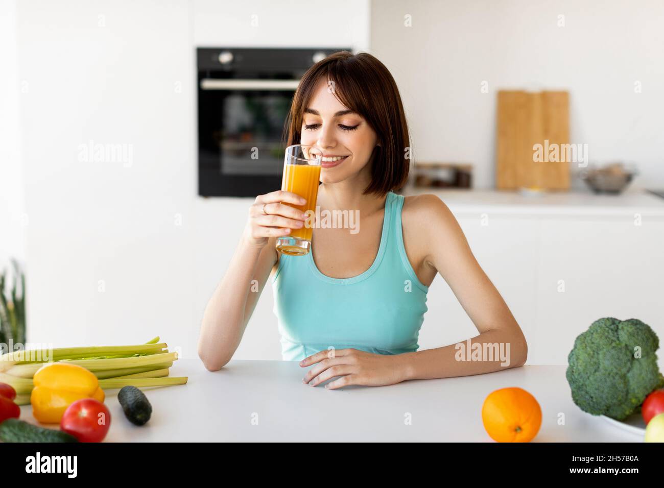 Dieta detox. Donna sottile bere succo d'arancia mentre cucinano sana cena di verdure, seduto in una cucina moderna e leggera Foto Stock
