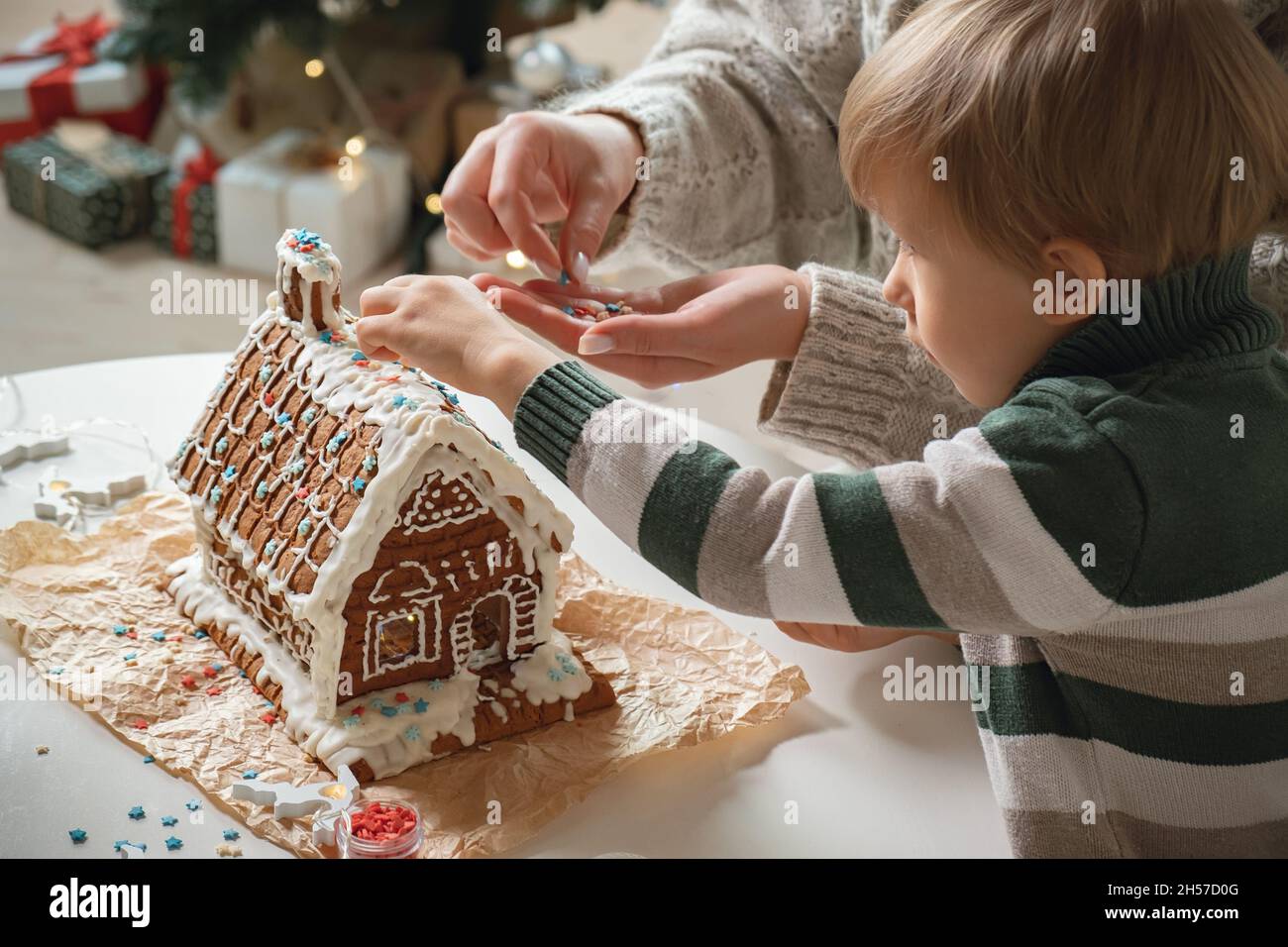 Ragazzino con madre che decora insieme casa di pan di zenzero di natale, attività di famiglia e tradizioni a Natale e Capodanno Foto Stock