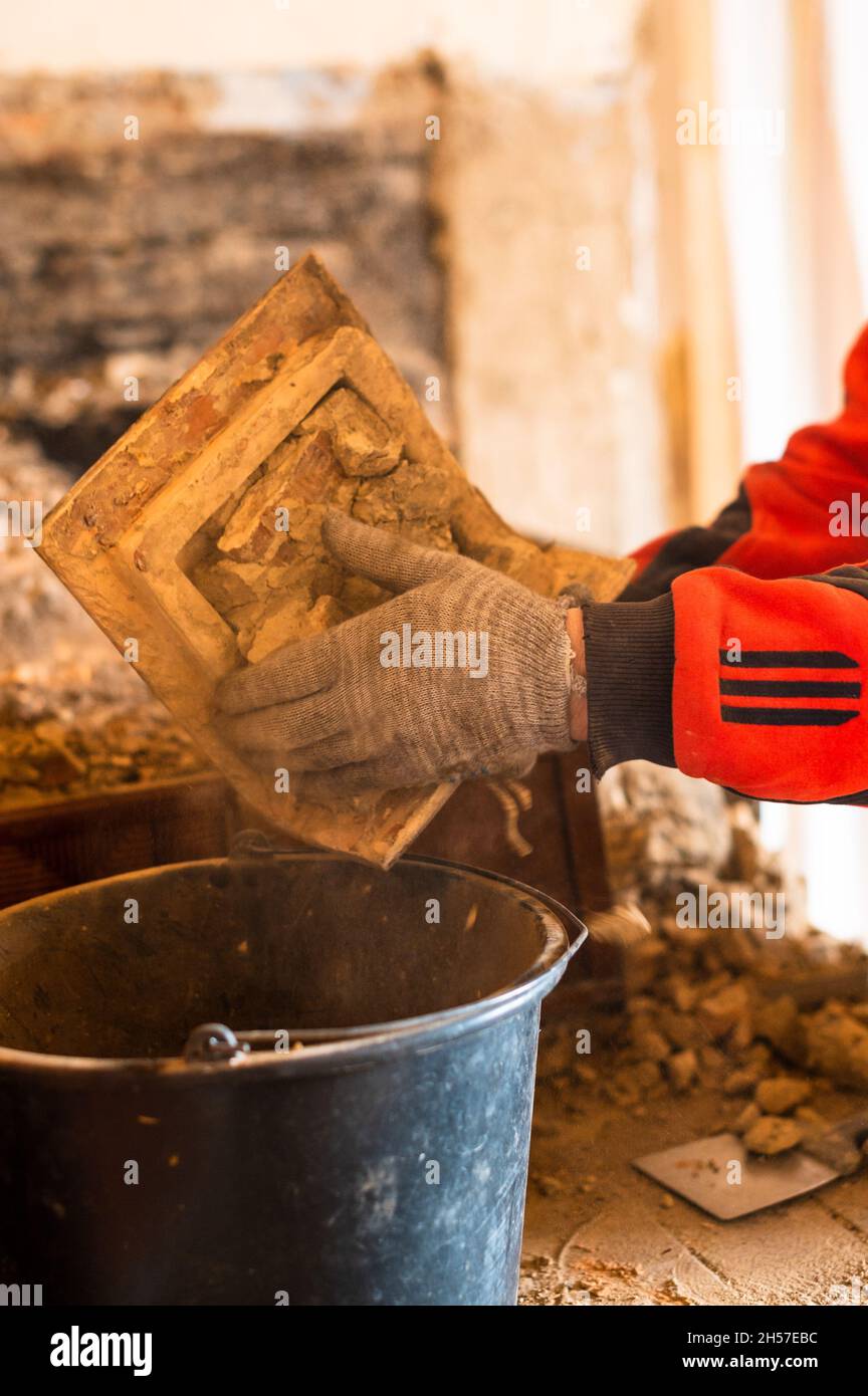 Una vecchia stufa di mattoni, mattone in fuliggine, smantellando la vecchia cucina con le sue mani, il padrone rotola via il mattone con le sue mani. Nuovo Foto Stock