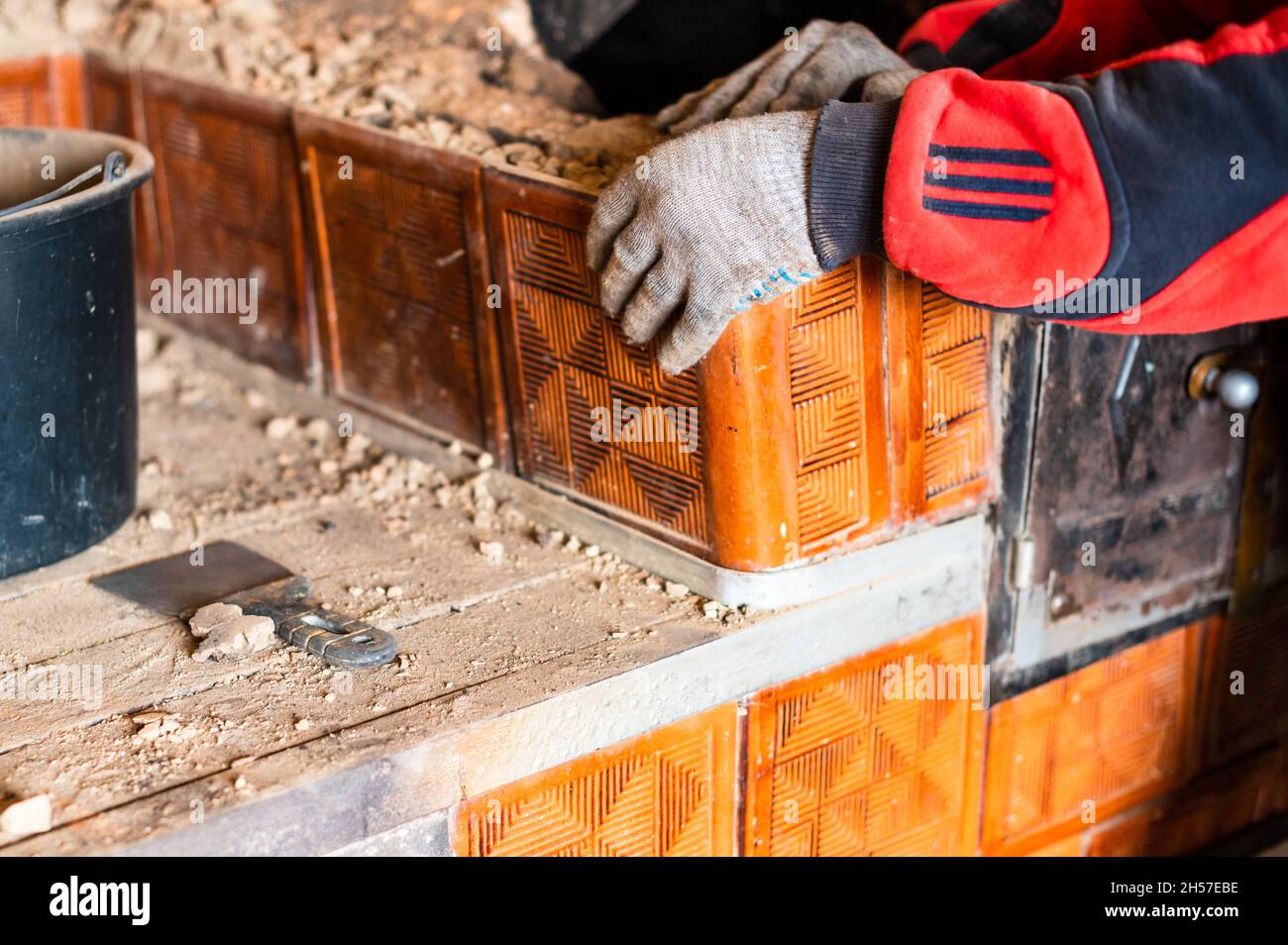 L'uomo distrugge una vecchia stufa di mattoni, mattoni neri in fuliggine, smantellando la vecchia cucina surface. Nuovo Foto Stock