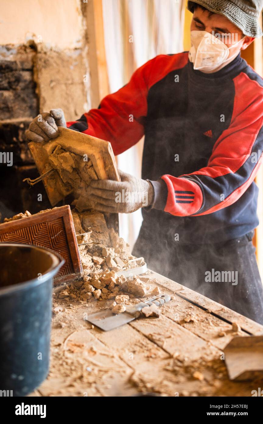 Una vecchia stufa di mattoni, mattone in fuliggine, smantellando la vecchia cucina con le sue mani, il padrone rotola via il mattone con le sue mani. Nuovo Foto Stock