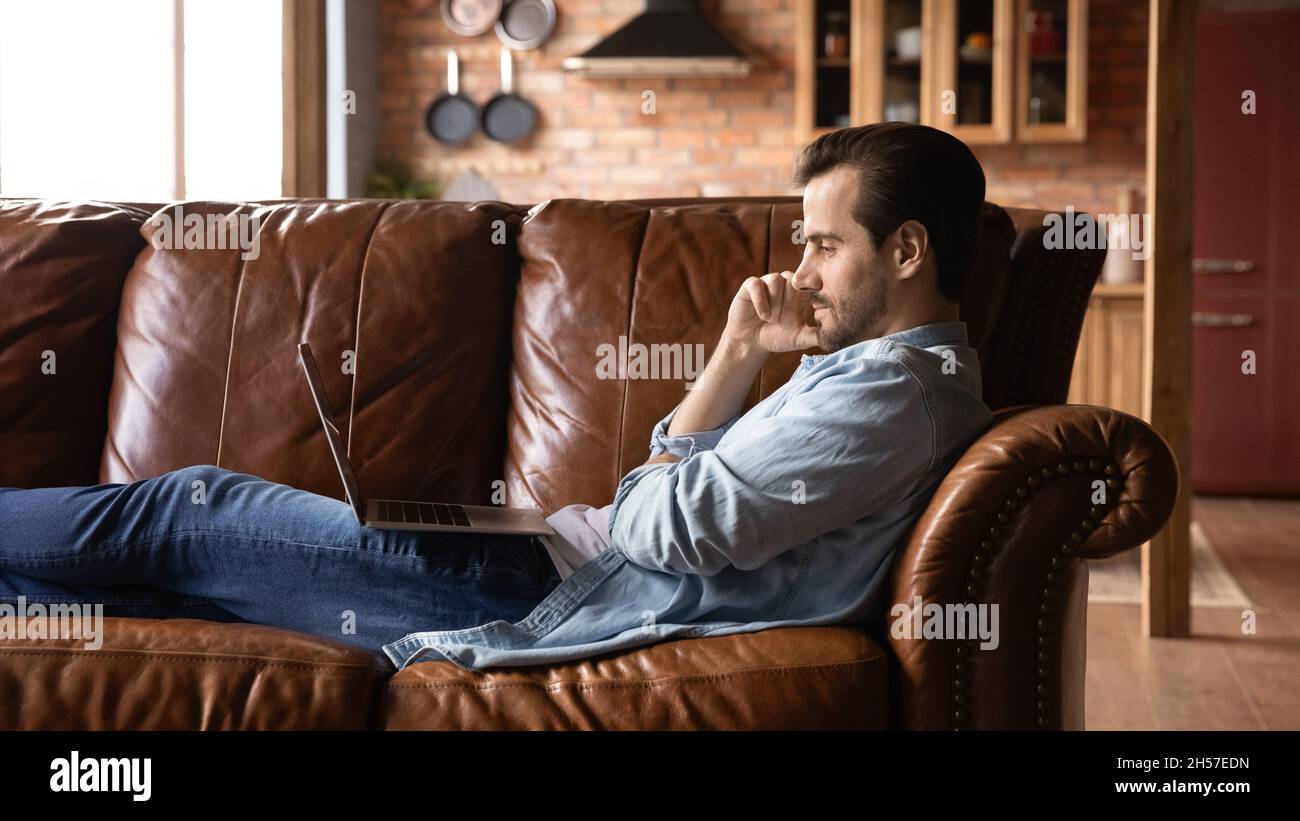 Rilassato riposo maschile casual sul divano con computer portatile in ginocchio Foto Stock