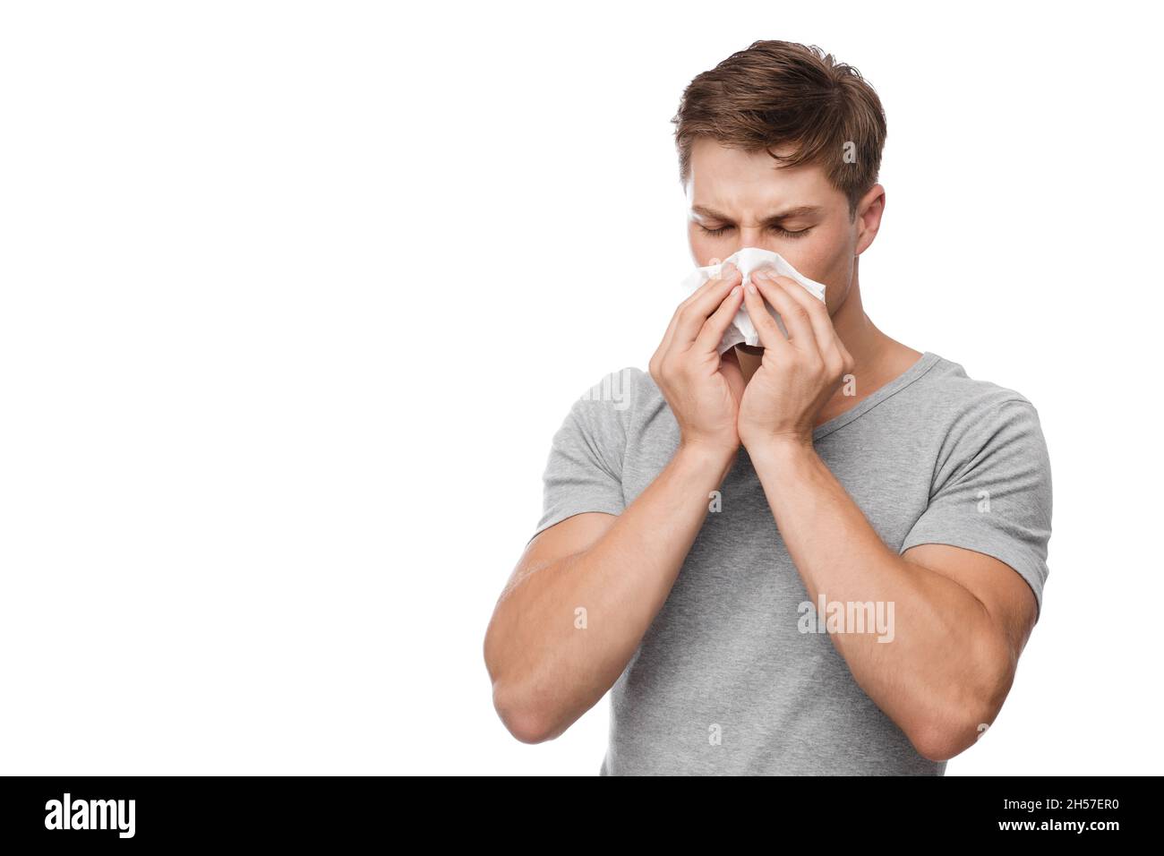 Infelice uomo millenario europeo attraente soffia il naso in tovagliolo e soffre di naso che cola Foto Stock