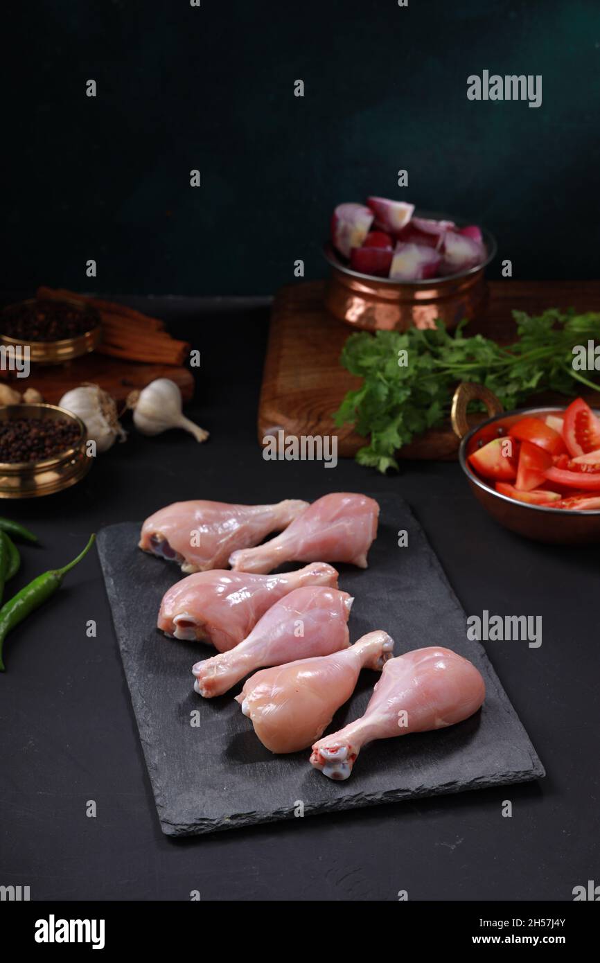 Bastone di tamburo di pollo crudo o pezzi di gamba disposti su foglio di grafite con ingredienti di cottura posti vicino. Foto Stock