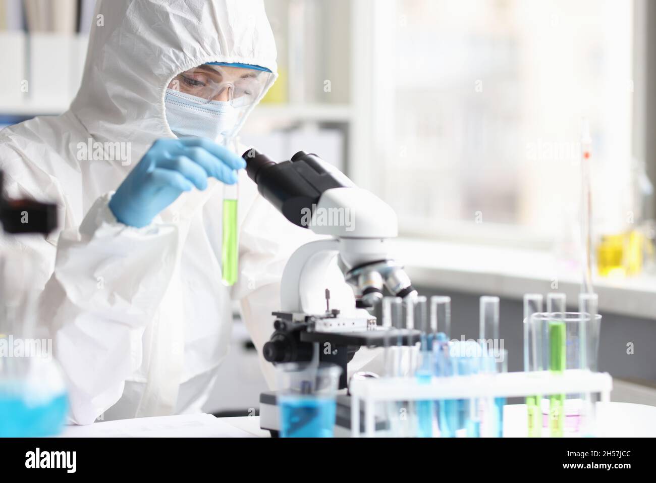 Chimico scienziato in tuta protettiva che tiene in laboratorio la provetta con liquido verde Foto Stock