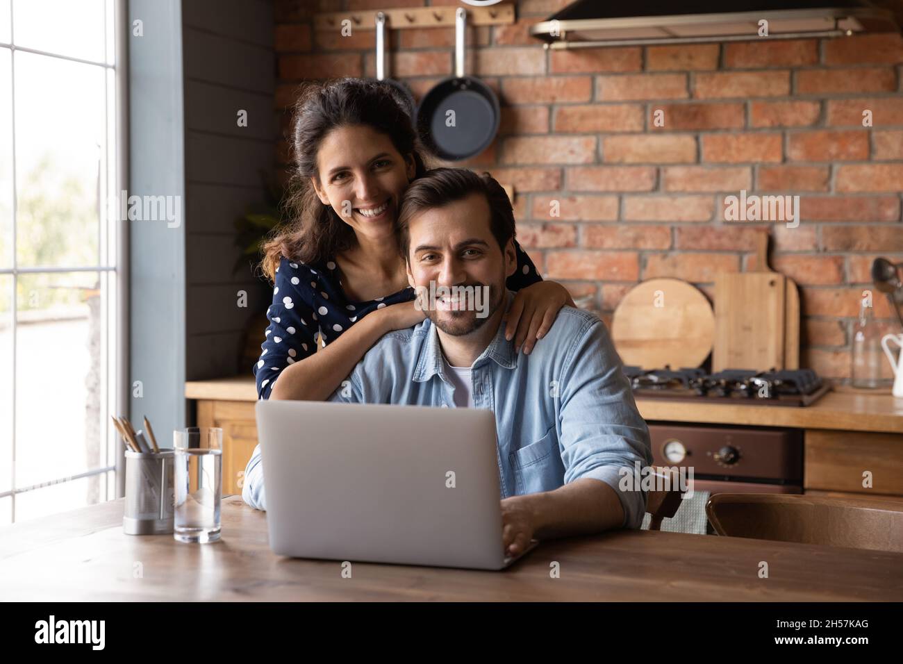 Felice giovane moglie abbracciare marito seduto al tavolo da computer Foto Stock