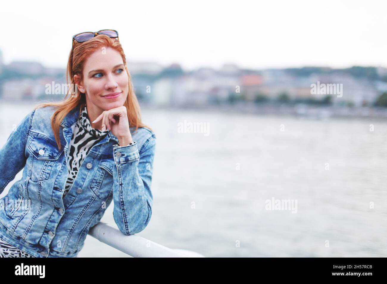 Giovane donna serena caucasica rossa che si posa in riva al fiume, guardando via Foto Stock