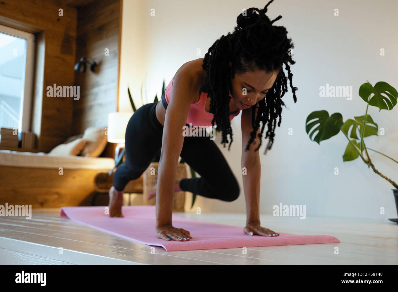 Forte bella ragazza di idoneità in vestiti di workout di atletica sta facendo un'esercitazione della tavola. Lei si sta allenando a casa nel suo salotto con interno accogliente. Foto Stock