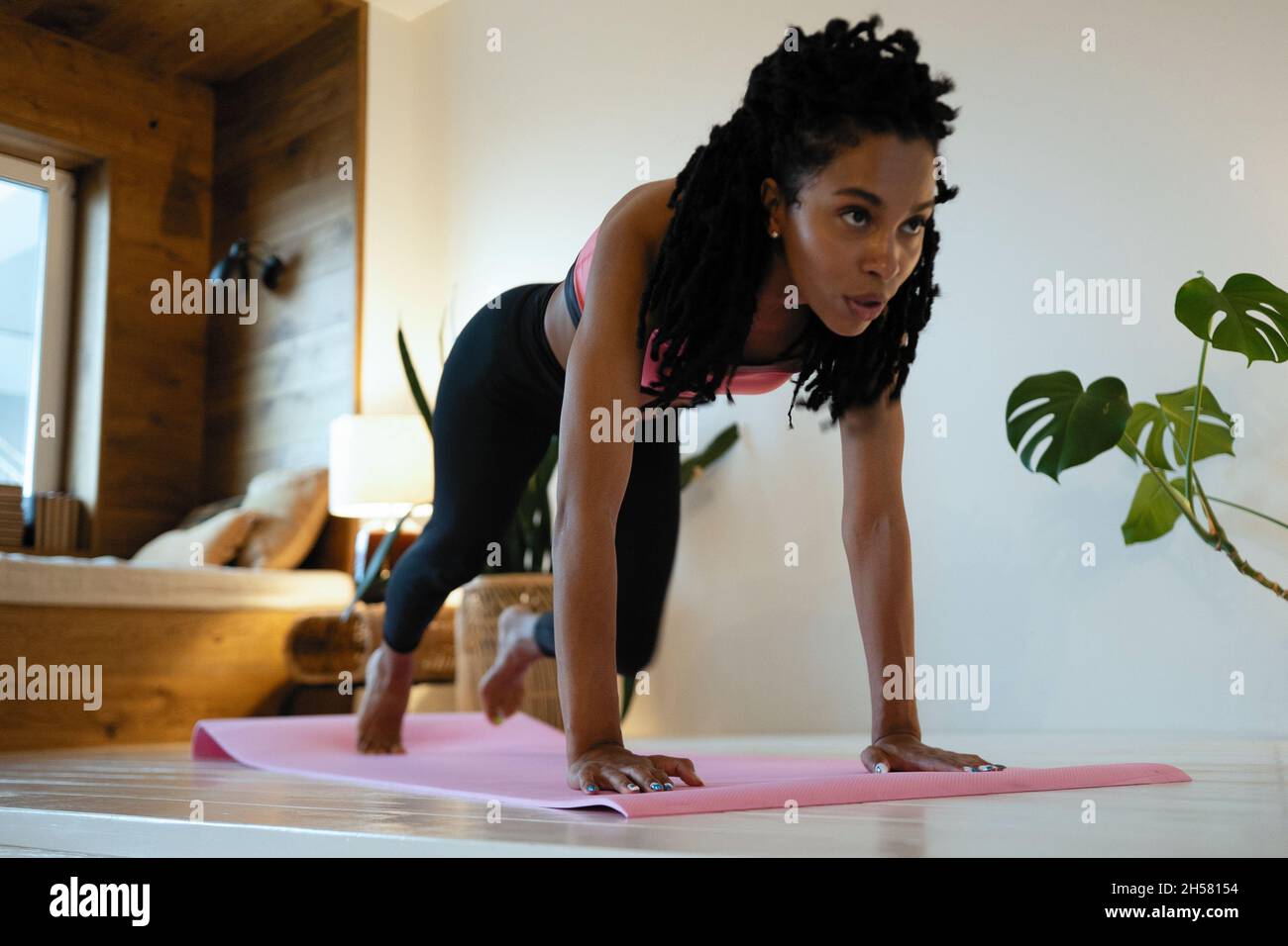 Forte bella ragazza di idoneità in vestiti di workout di atletica sta facendo un'esercitazione della tavola. Lei si sta allenando a casa nel suo salotto con interno accogliente. Foto Stock