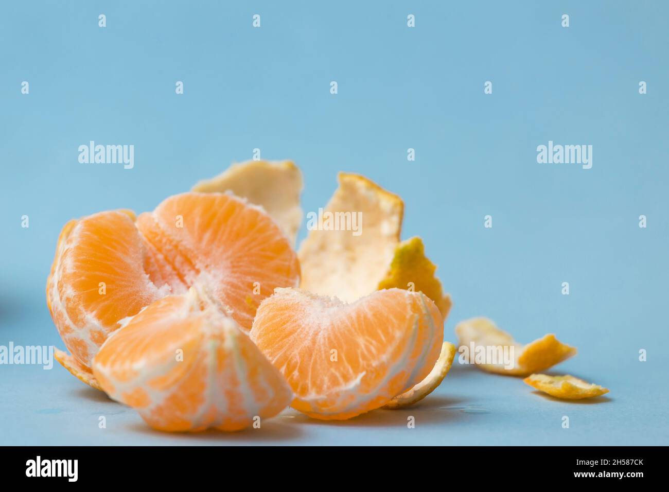 mandarino sbucciato e suddiviso in segmenti, su sfondo blu, agrumi sani Foto Stock