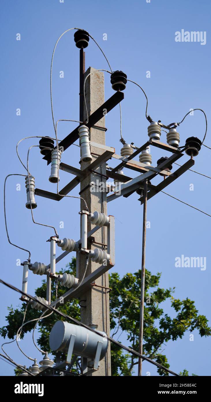 Primo piano linea di alimentazione ad alta tensione su uno sfondo di cielo blu in una giornata di sole. Polo elettrico, polo con fili, cavi sotto tensione, trasformatore.Urban industriale l Foto Stock