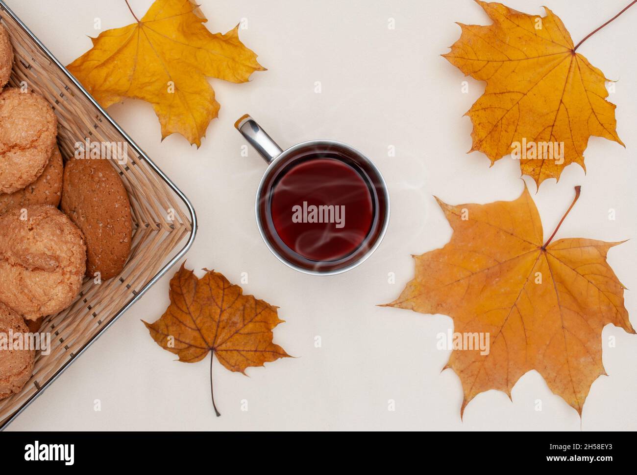 piatto di foglie di acero giallo autunno, tazza con tè caldo, cestino con biscotti su sfondo avorio Foto Stock