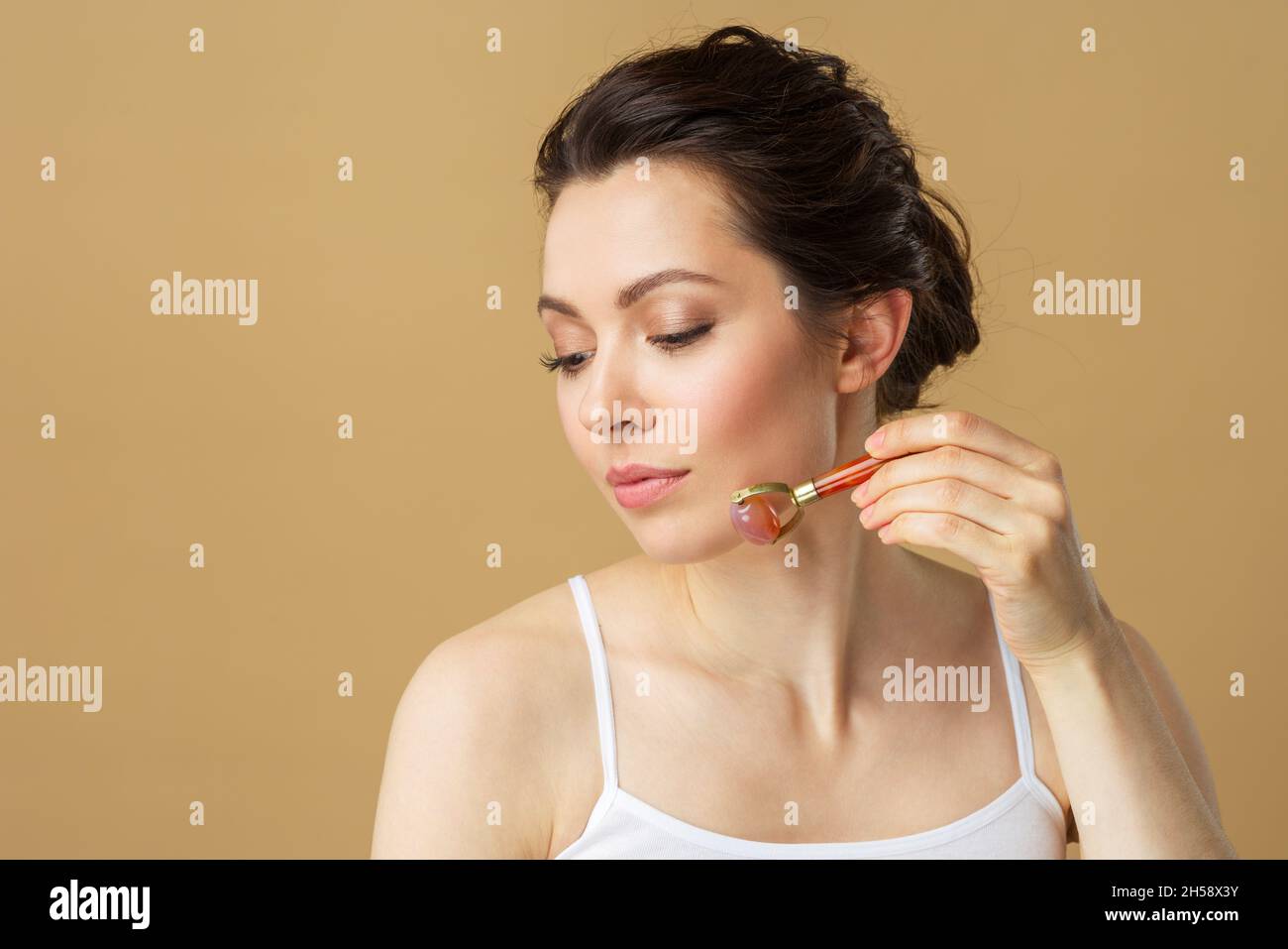 Ritratto di una giovane donna con un rullo per massaggio facciale in quarzo rosa naturale Foto Stock