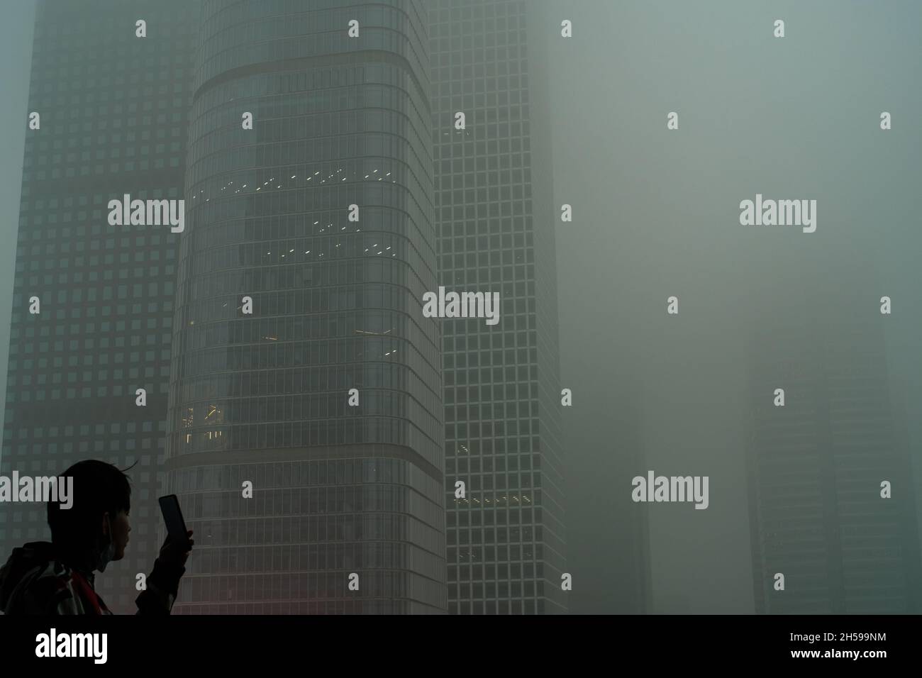 Un giovane uomo usa il suo cellulare per fotografare i grattacieli avvolti in smog severo nel CBD di Pechino, Cina. 06-Nov-2021 Foto Stock