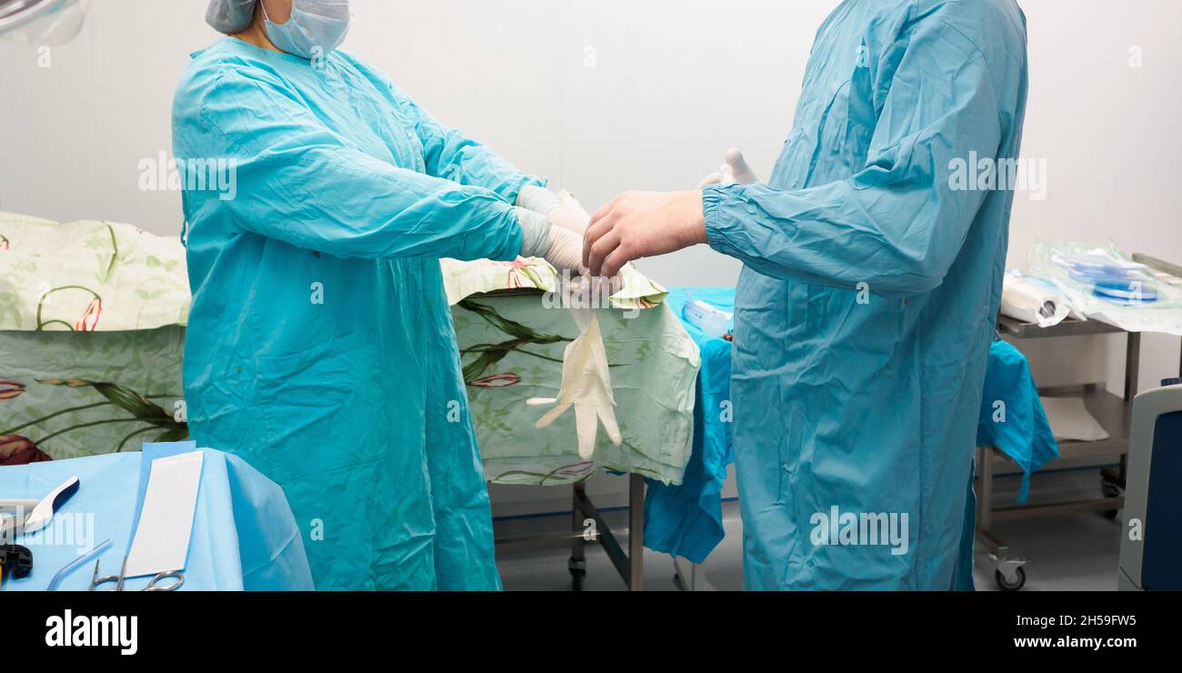 Un assistente infermieristico aiuta il chirurgo a indossare guanti in lattice prima dell'intervento chirurgico. Vestiti sterili per i medici durante l'intervento chirurgico. Foto Stock