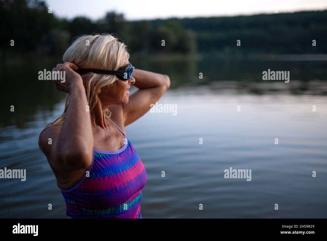 Ritratto di attiva donna anziana nuotatore in piedi e indossare occhiali all'aperto in lago. Foto Stock