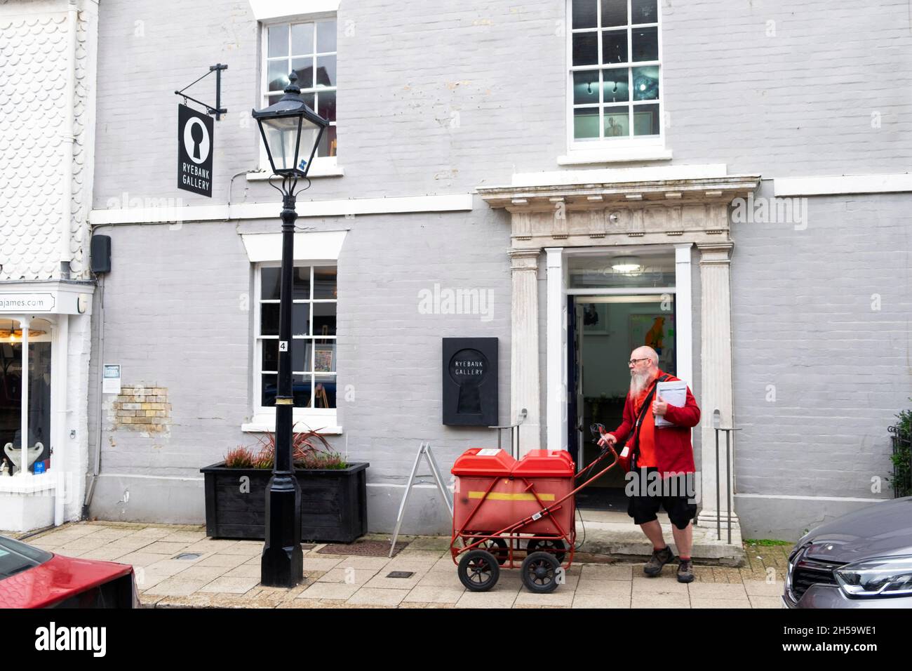 Royal mail postman con barba bianca che consegna lettere con carrello postale rosso fuori casa Rye East Sussex Inghilterra Regno Unito in autunno 2021 KATHY DEWITT Foto Stock