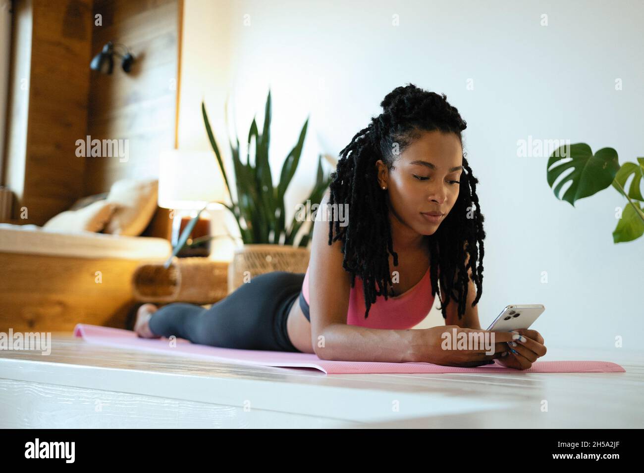 Giovane donna sportiva dopo aver praticato lo yoga, fare esercizio, rilassarsi sul tappeto yoga, inviare SMS sullo smartphone Foto Stock