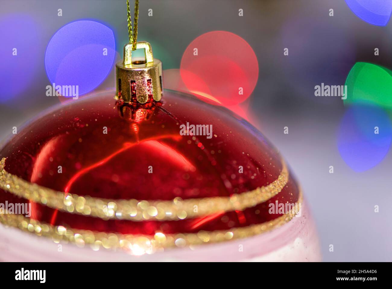 Sfera di natale di colore rosso davanti alle luci dell'albero di natale, primo piano, concetto di festa, macro fotografia Foto Stock