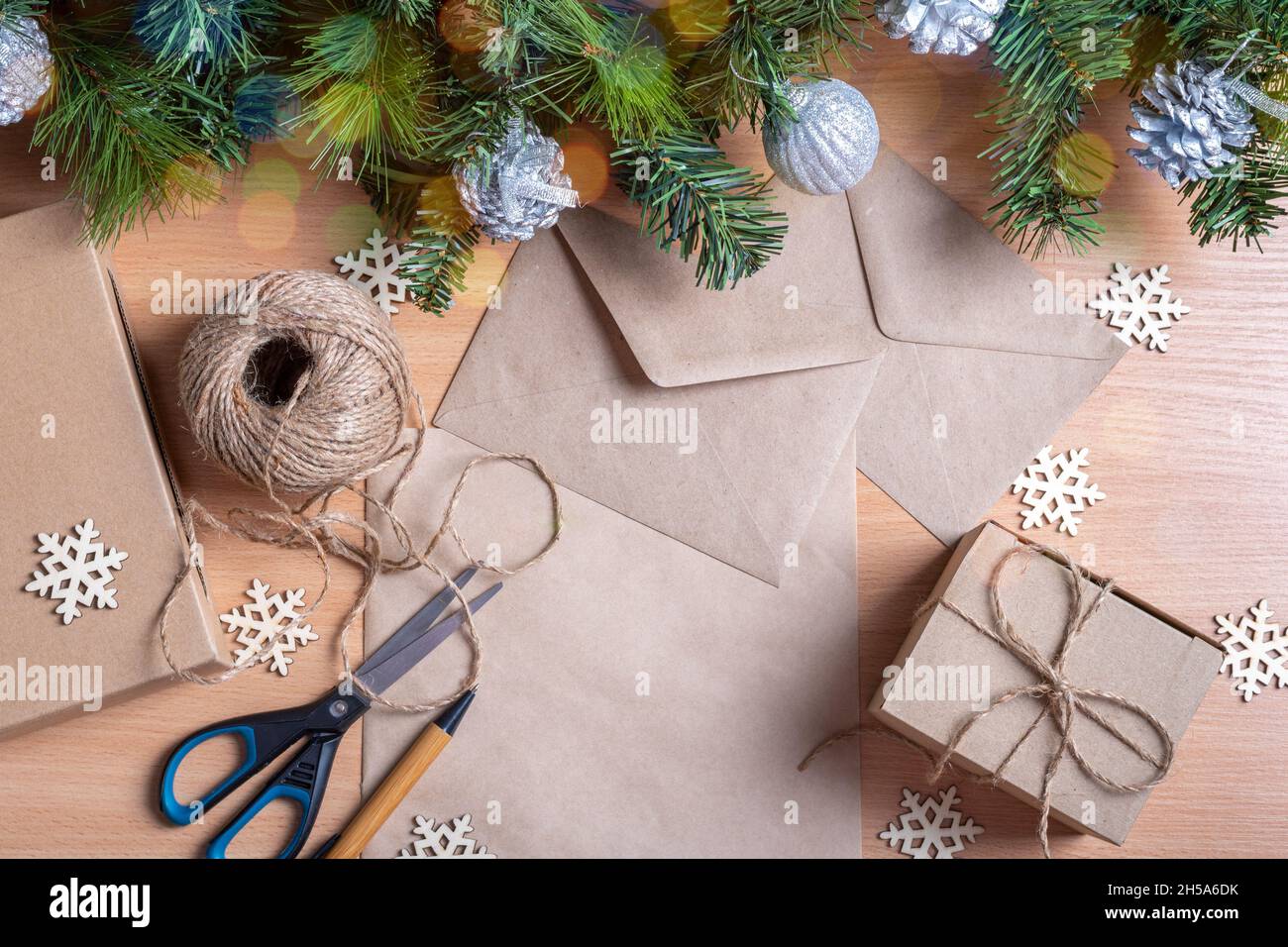Concetto di Natale senza sprechi. Regali in scatole fatte a mano, carta riciclata, busta, spago, forbici, rami artificiali di abete rosso e fiocchi di neve in legno, bo Foto Stock