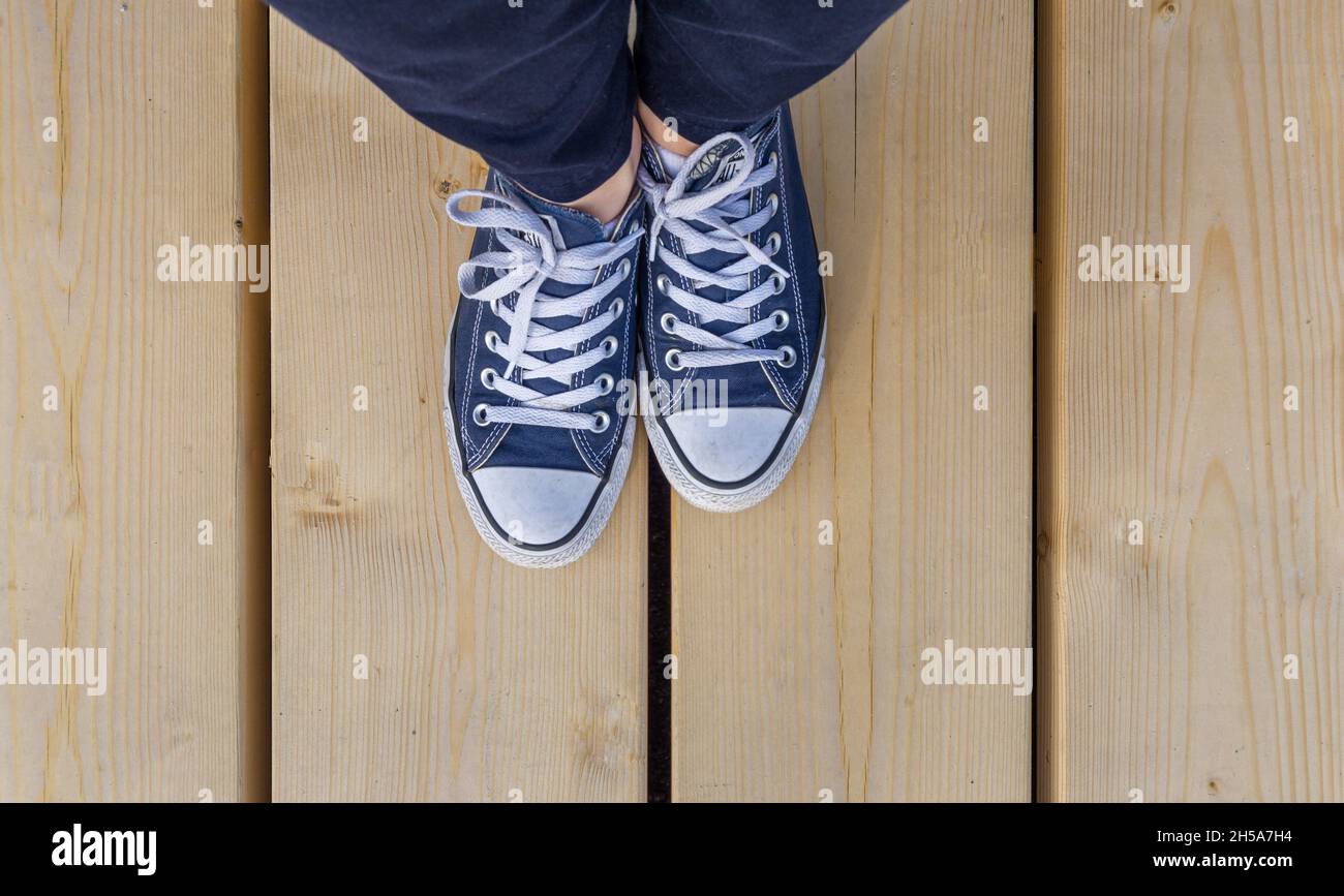 Sodertalje, Svezia - 11 maggio 2021: Un paio di ragazze tutte le sneaker star dal punto di vista degli uccelli con gambe visibili in pantaloni blu su pavimento in legno Foto Stock