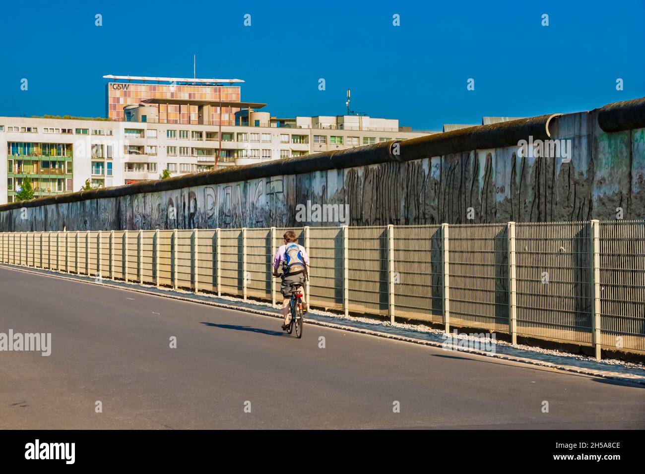 Vista pittoresca di un ciclista sulla famosa strada Niederkirchnerstraße e una sezione preservata del muro di Berlino sullo sfondo a Berlino,... Foto Stock