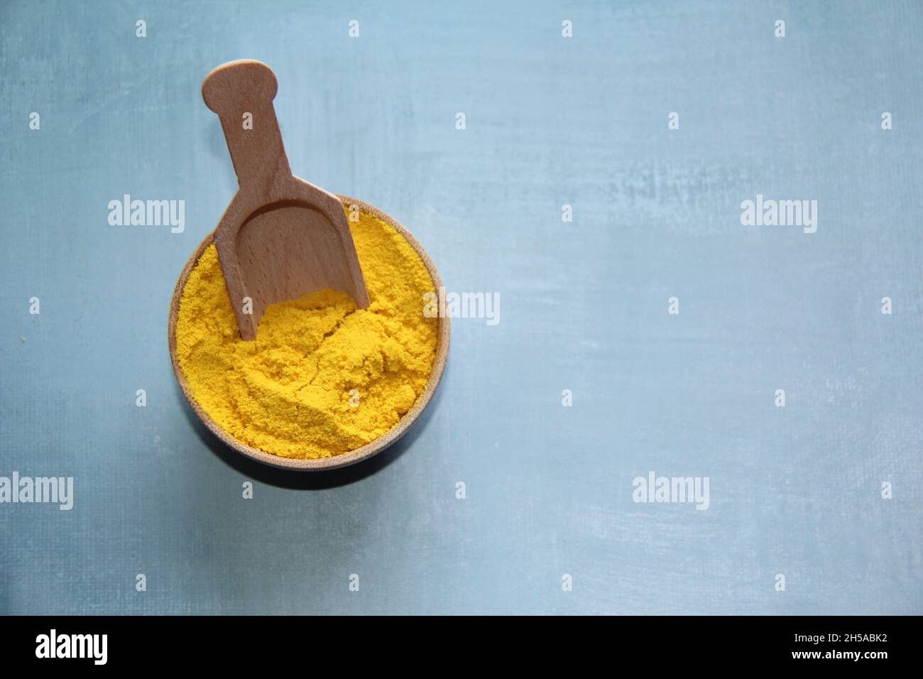 Mostarda in polvere in una ciotola di legno con un misurino di legno su un vecchio tavolo di legno. Foto Stock