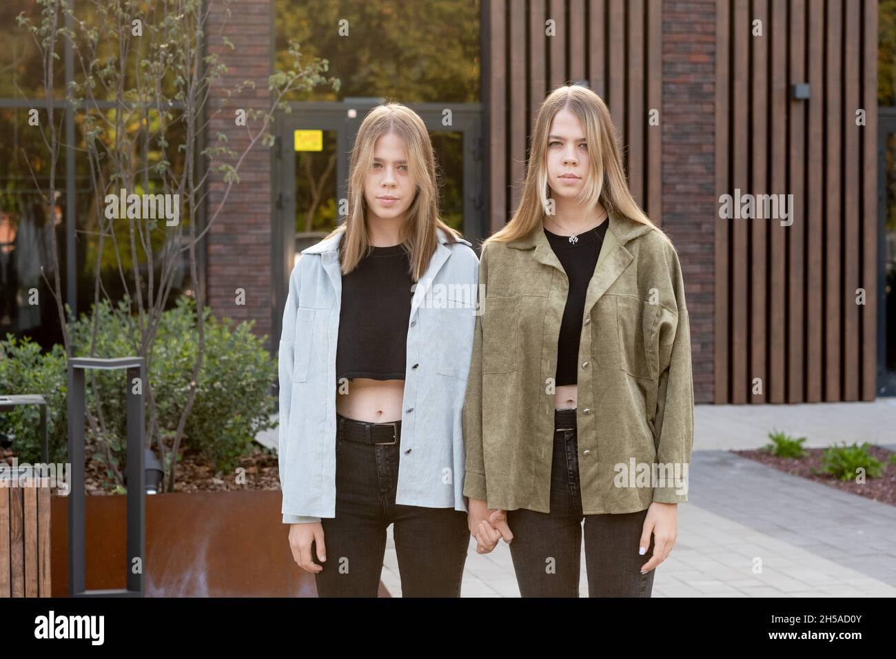 Grave teenage femminile gemelle in casualwear in piedi contro l'esterno edificio di fronte alla macchina fotografica Foto Stock