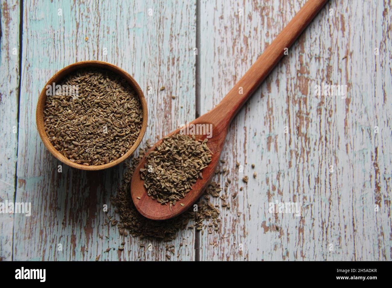 Semi di finocchio intero, finocchio, finocchio, finocchio di Firenze, passera o finocchio di testa (Foeniculum vulgare Mill) in una ciotola e cucchiaio di legno. Su un vecchio tavolo. Foto Stock