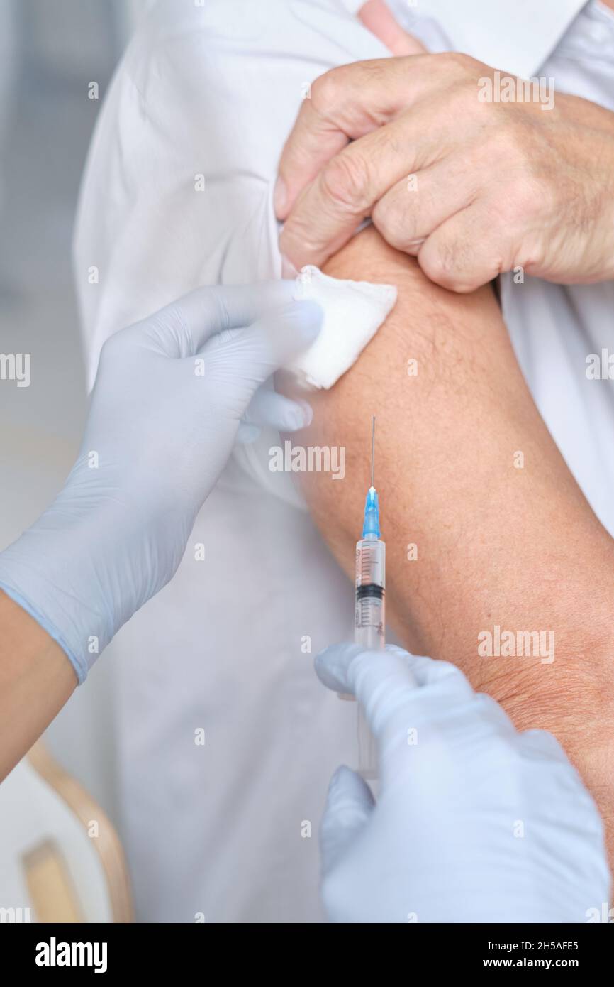Primo piano del paziente che riceve un'iniezione nel braccio da parte dell'infermiere durante la procedura medica Foto Stock