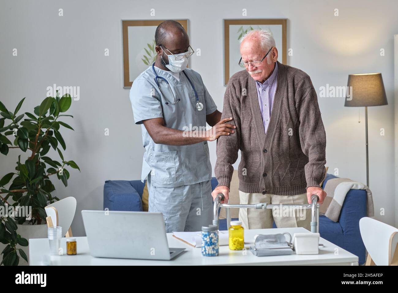 Uomo anziano che usa gli escursionisti mentre visita il suo medico all'ospedale, e medico che lo esamina Foto Stock