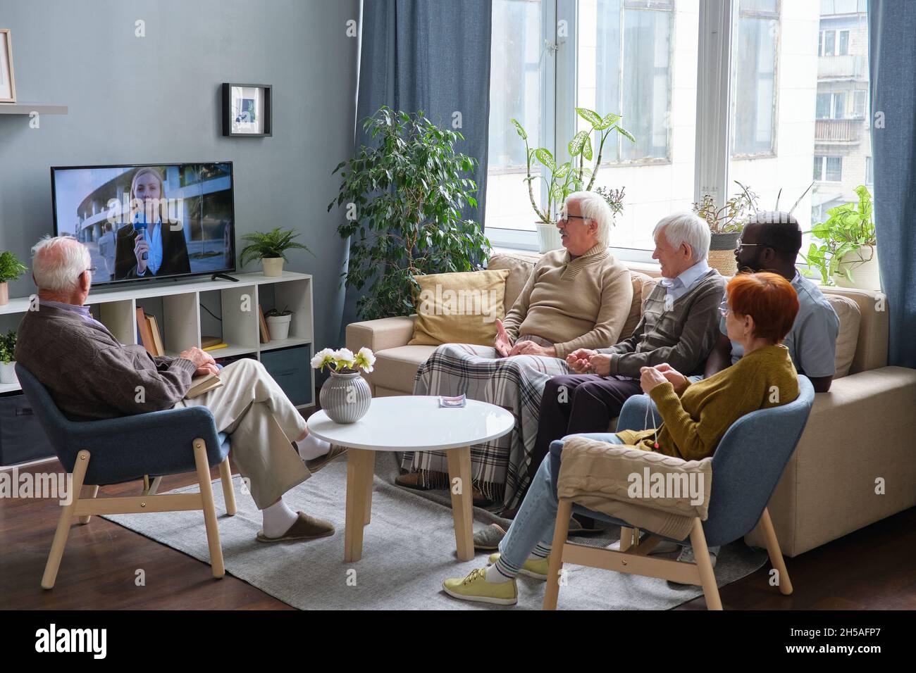Gruppo di persone anziane che riposano sul divano nel soggiorno e guardano le notizie insieme in TV Foto Stock